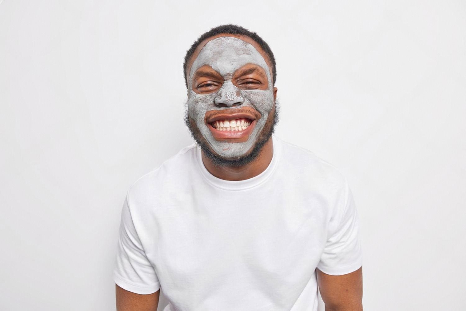 Man smiling with a cosmetic clay mask on his face during a skincare session
